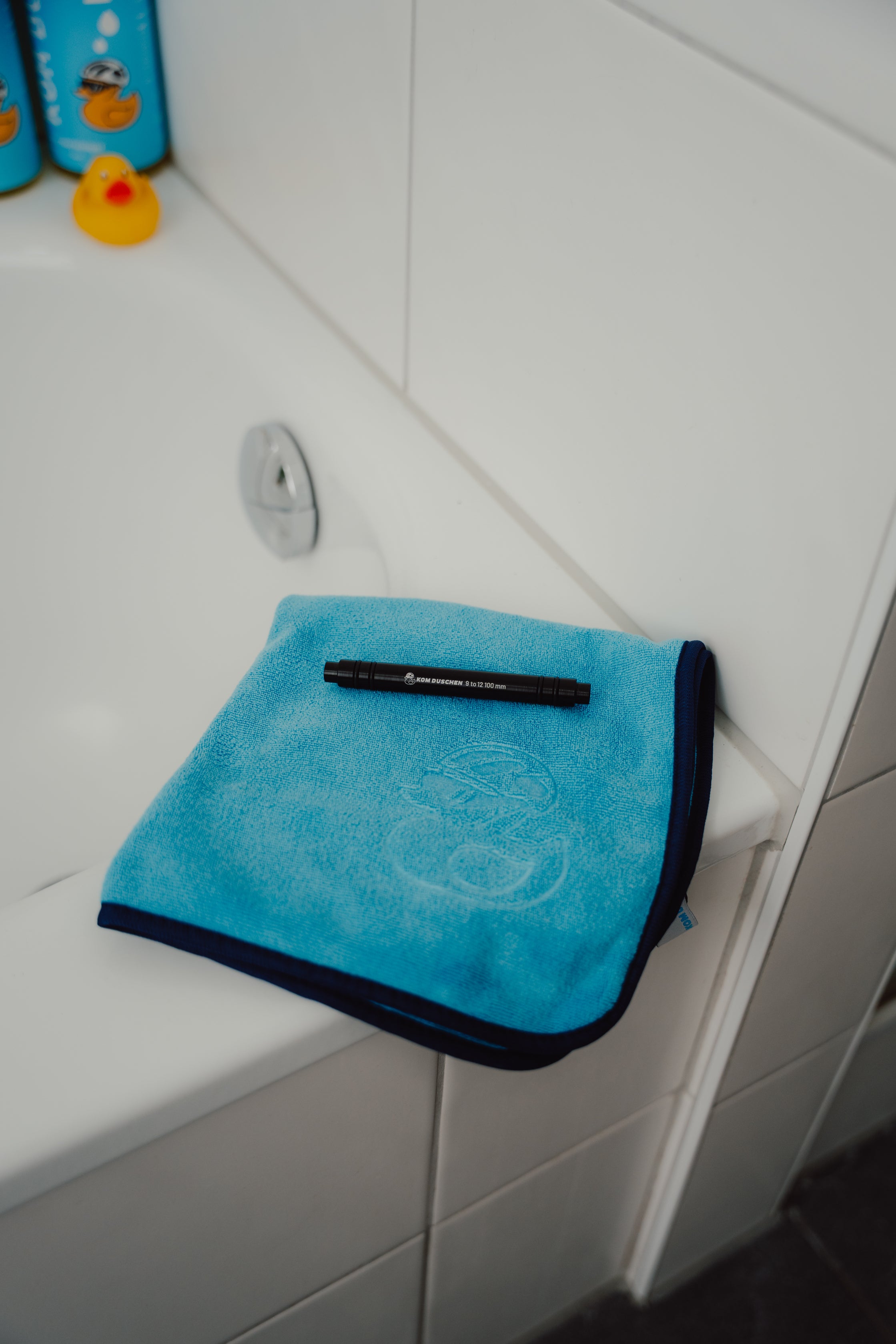 Ein blaues Mikrofasertuch – Reinigungstücher 400 g/m² (4 Stück) – liegt gefaltet am Rand einer weißen Badewanne, auf der ein schwarzer Filzstift liegt. Im Hintergrund sind Flaschen und eine Gummiente zu sehen.