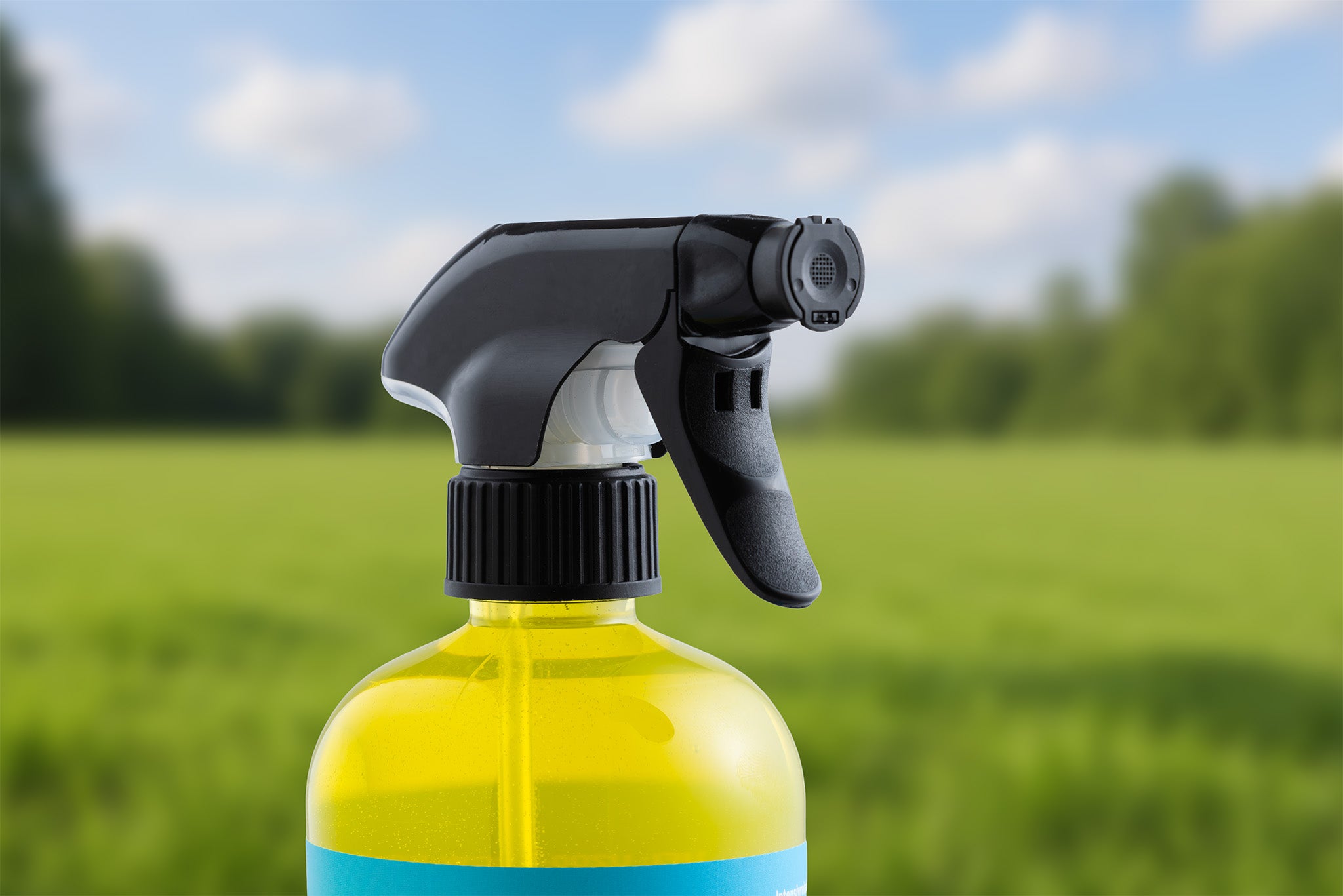 Nahaufnahme einer Sprühflasche mit gelbem Intensivreiniger - gebrauchsfertig in Gelform, mit schwarzer Düse, vor einem unscharfen Hintergrund mit grünem Gras und Bäumen.